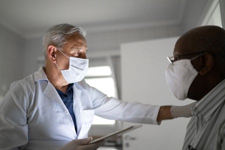 An older male doctor talks to a patient while holding an electronic tablet.