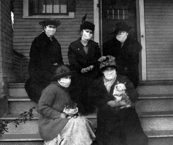 Historical image of masked women sitting on porch with cats.