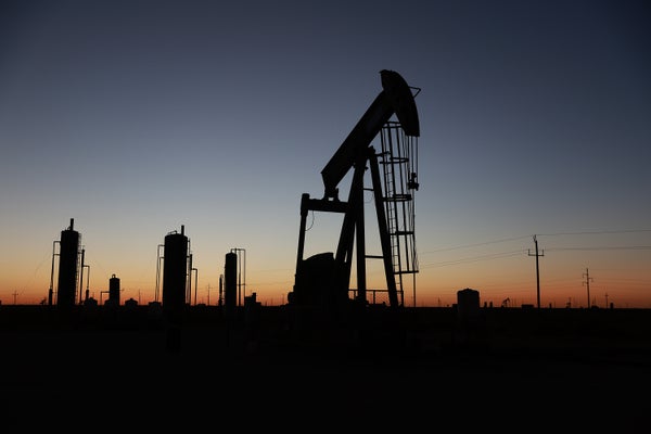An oil pumpjack during sunset with petrolium containers on the horizon.