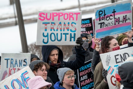 A crowd of people hold signs supporting trans youth.