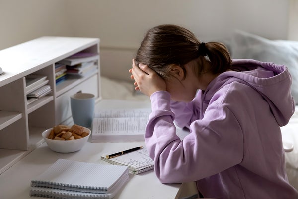 Stressed teen a desk in purple hoodie with head in hands