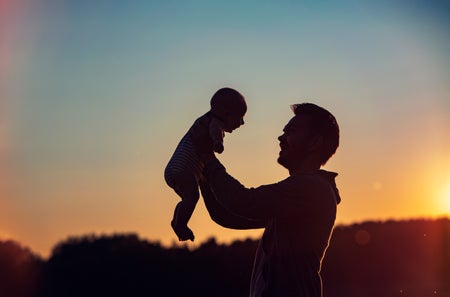 Father lifting son silhouette in front of sunset