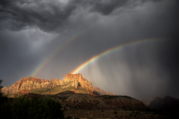 Double rainbow in dark clouds above massive rock formations