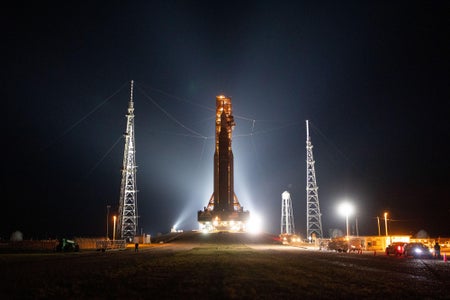 Rocket silhoutted against night sky by bright lights