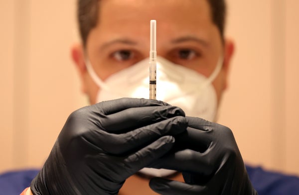 Close up of masked heathcare worker with gloved hands holding a syringe in front of their face