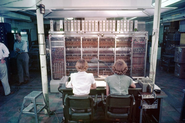 Women seen from behind facing a bank of electronics.