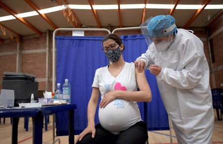 Pregnant woman in a mask with a valentine on her T-shirt gets vaccinated in Colombia.