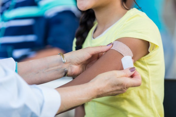 Doctor applies bandage to preteen girl's arm following an immunization.