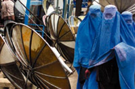 Afghan women in Kabul pass a shop selling satellite dishes