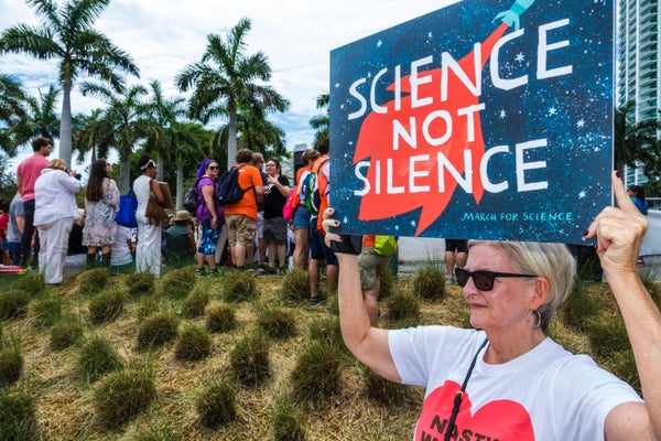 A woman holds up a sign that says "Science Not Silence""