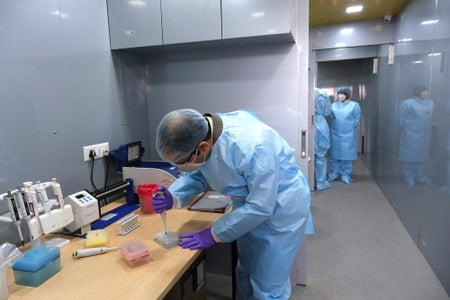 A health care worker in blue PPE processes COVID test samples.