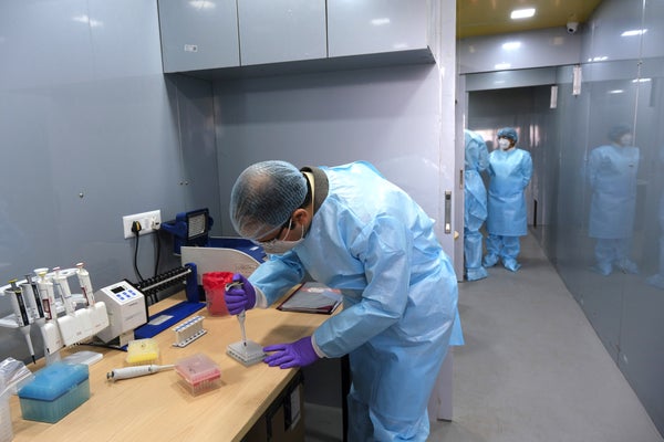 A health care worker in blue PPE processes COVID test samples.