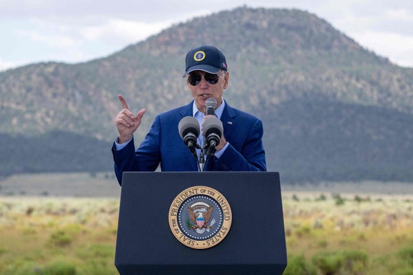 President Biden with baseball cap and sunglasses speaking in front of Arizona Landscape.