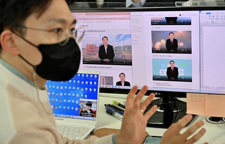 A young man sits in front of multiple computer screens.