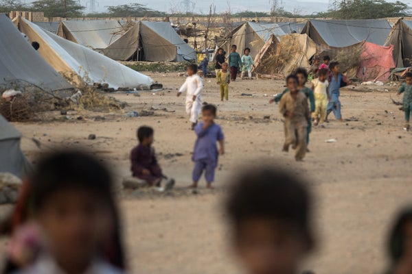 Children play at a refugee camp with tents in the background.