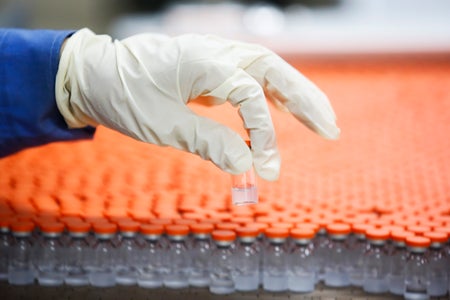 A gloved hand pulls a small vaccine vial from an a production line.