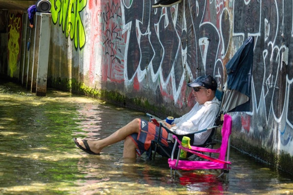 A man sits in a chair in a creek to cool off.