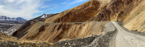 A panoramic view of the Pretty Rocks landslide area shows the road and construction vehicles and snow capped mountains in the distance.