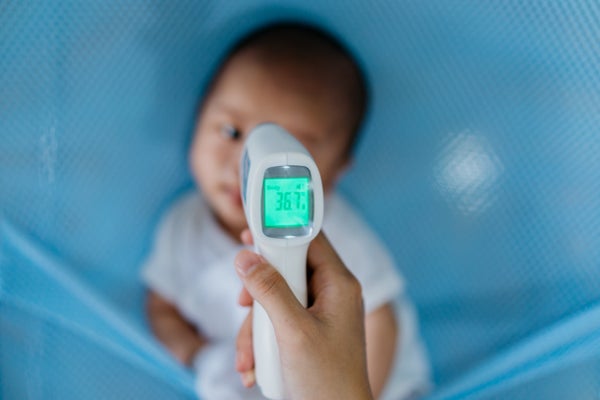 infrared thermometer being held in focus, checking temperature of infant seen out of focus behind thermometer
