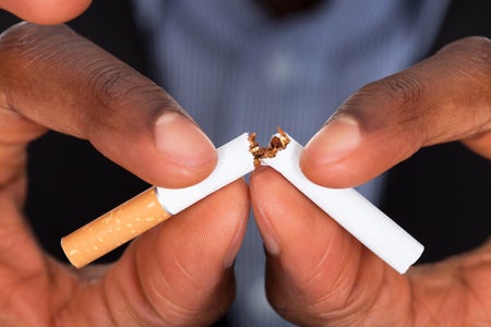 Two hands break a cigarette in half.