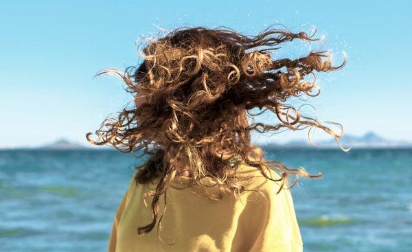 Blonde woman shaking her head with curly and messy hair flying over against sky line and sea.