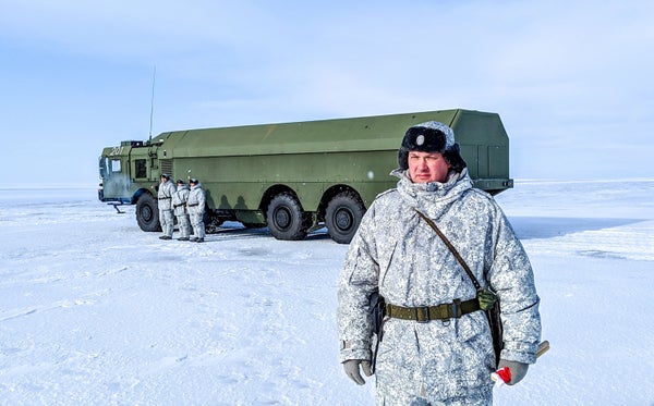 Russian officer in foreground of a green tank in the arctic with 3 soldiers in the background.