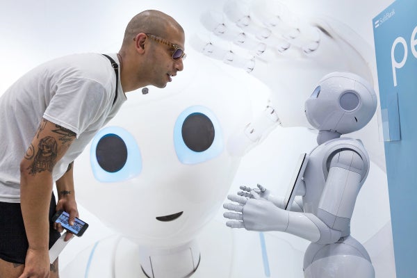 A man leans down to talk to a small, white robot