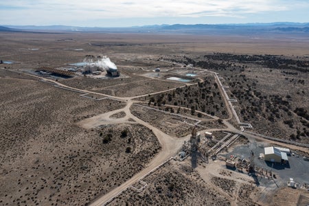 Aerial view of a geothermal plant infrastructure with smoke rising in Utah desert.