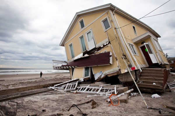 A person walking on a beach is seen by a damaged home, leaning to one side after the foundation was destroyed by storm surge in Queens, NY