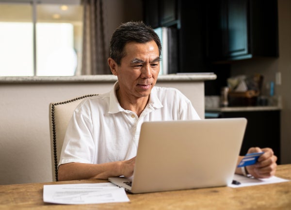 Asian man at desk with laptop holding a credit card