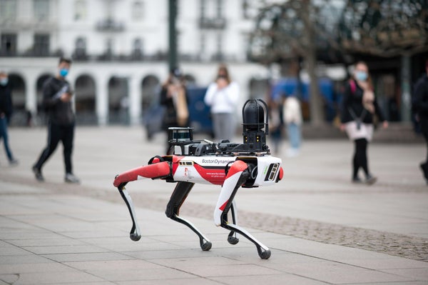 A robotic dog walks across a marketplace, observed by curious passersby.