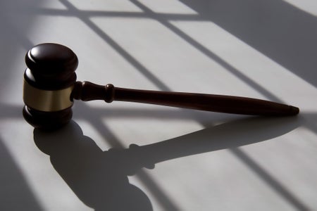 Enlongated shadows resembling jail cell bars cast over a judge's wooden gavel