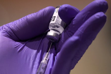 Covid vaccine and syringe held in medical worker's gloved hand.