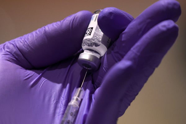 Covid vaccine and syringe held in medical worker's gloved hand.