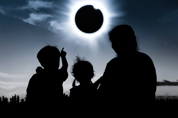 Silhouette of child pointing to solar eclipse next to another child and adult