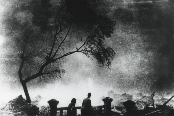 People seen in silhouette walking in foreground against a hazy background of smoke, destroyed buildings and vegetation