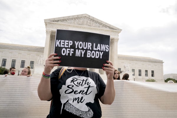 Activist holds "Keep Your Laws Off My Body" sign on steps of Supreme Court.