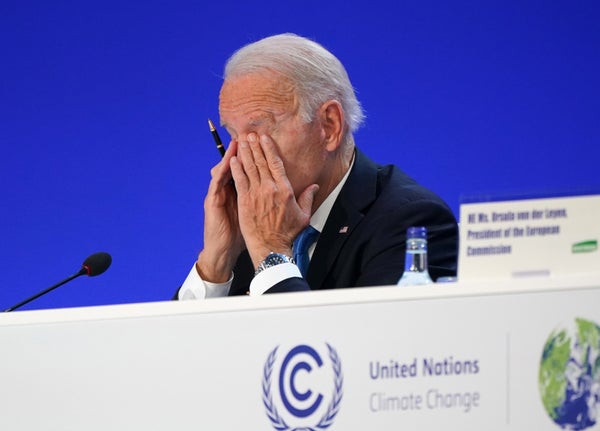 Joe Biden rubs eyes with both hands while seated at table