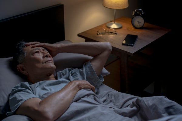 Asian man lying in bed awake from insomnia
