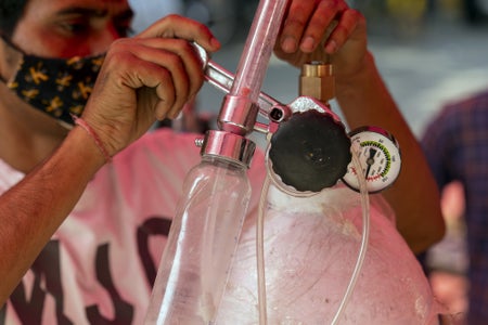 A man in a mask adjusts the controls on an oxygen cylinder.