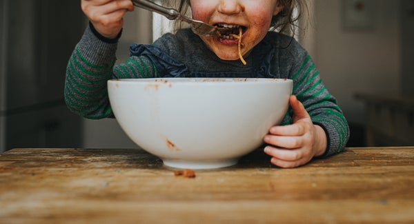 Child eating spaghetti from a white bowl.