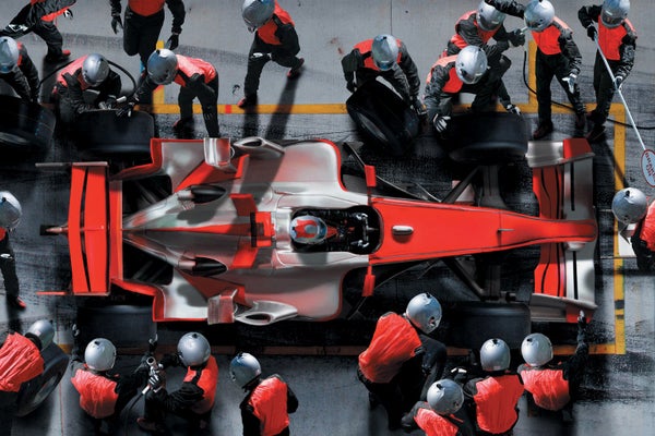 Red race car surrounded by mechanics wearing helmets.