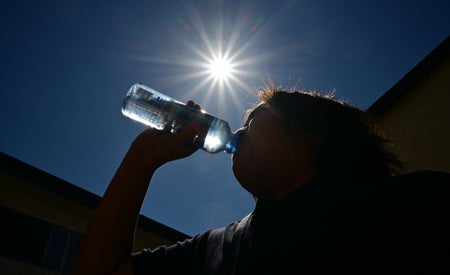 A woman sips water from a bottle against scorching sun star in the sky