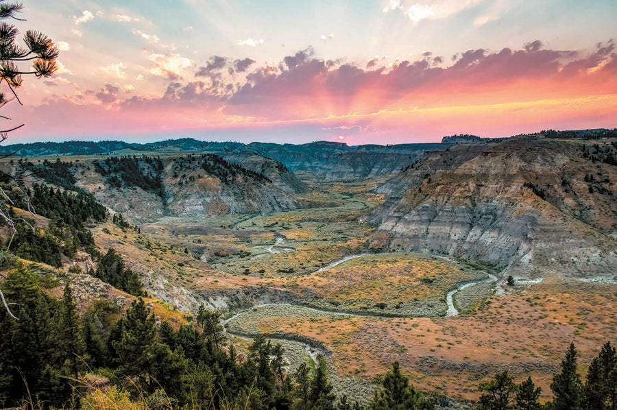 A wide view of a desert mountain and canyon landscape at sunset.