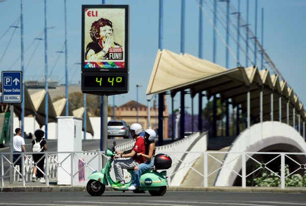 A green scooter is driven past a street thermometer reading 44 degrees Celsius.