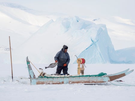 Fisherman with freshly caught fish in a small boat surrounded by icy waters and glaciers in Greenland.