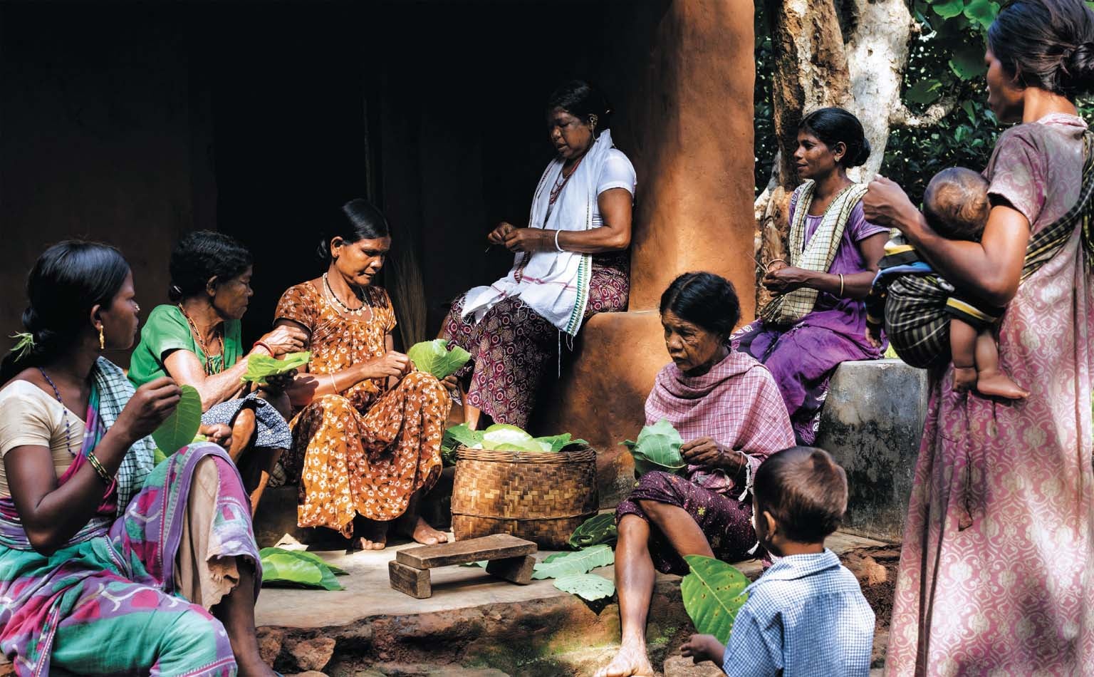 Group of people stitching leaves from a sacred Sal tree into bowls.
