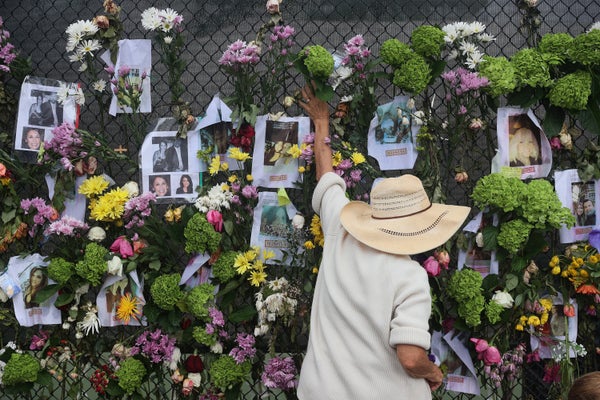 A person reaches up to add flowers to a memorial.
