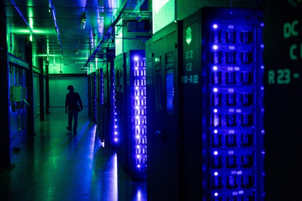 An engineer is shown in silhouette in a server room glowing in green and blue light.