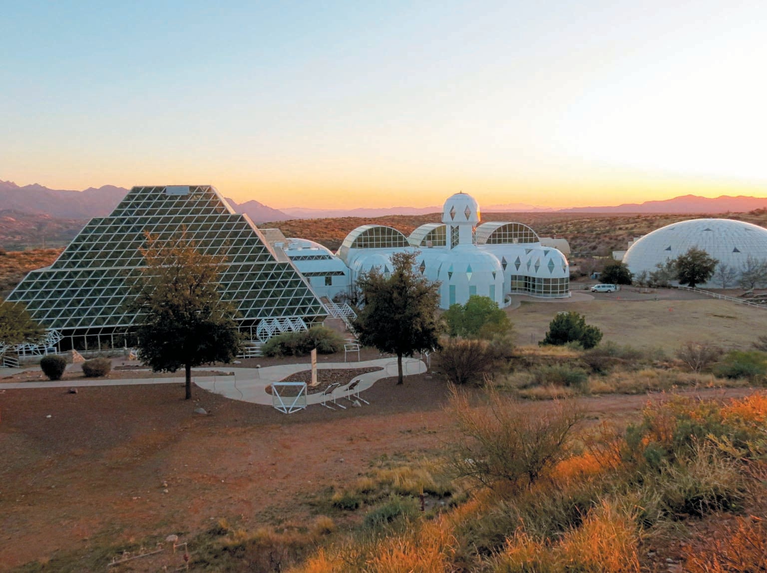 White geometric shaped buildings, identified as “The Biosphere 2 research facility” set in desert landscape.